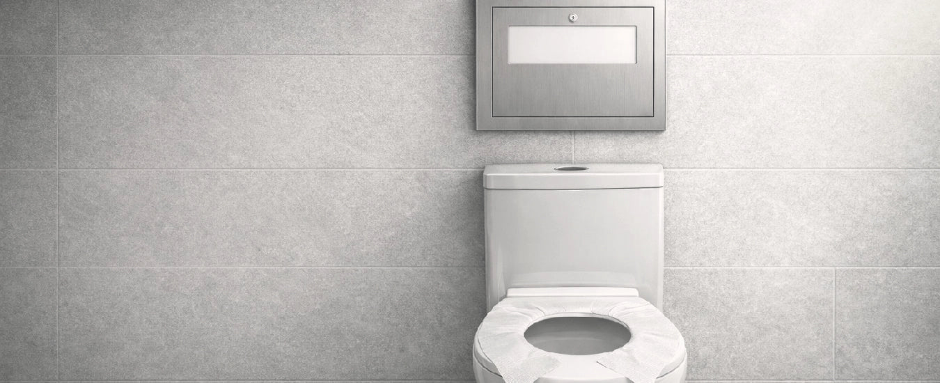 Image of White toilet with disposable seat cover in modern washroom with gray tiled walls and stainless steel dispenser