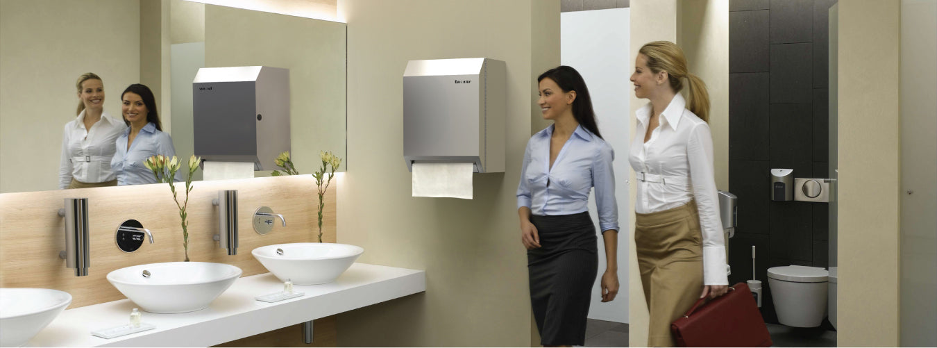 Image of Modern washroom with wall-mounted paper towel dispenser, sleek sinks, and women walking by for hygiene convenience